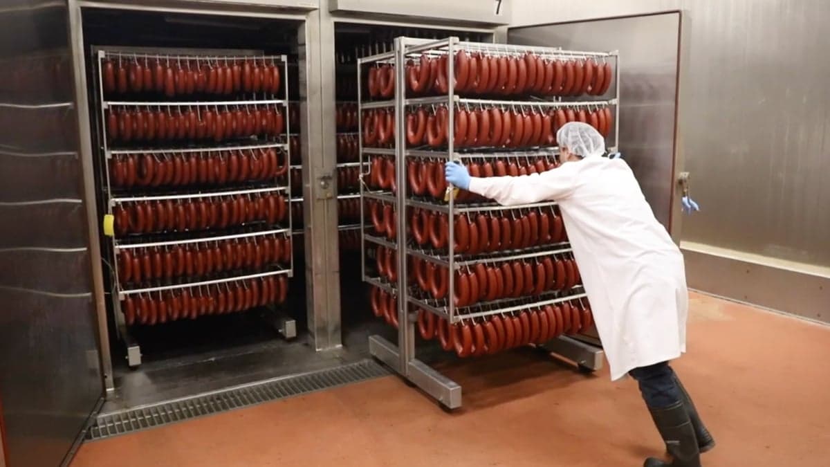 A worker in a white coat pushing a rack of beef sujuk rings into the curing chamber at the Nema plant